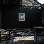 Un bombero en las ruinas carbonizadas de una casa, mirando con asombro la pintura de "The Crying Boy", que cuelga intacta en una pared quemada.