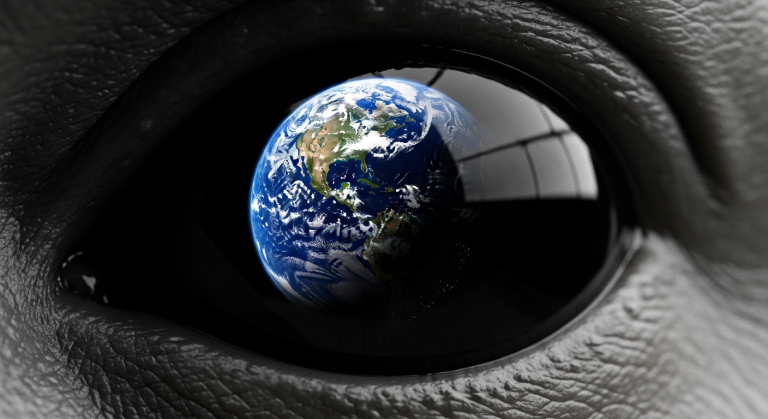 Un primer plano extremo de un ojo de un extraterrestre Gris, grande y negro, en el que se refleja el planeta Tierra, simbolizando su enfoque y agenda en nuestro mundo.