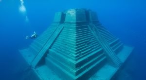 Vista submarina gran angular del Monumento de Yonaguni en Japón, mostrando sus inmensas terrazas de piedra y un buzo para escala.