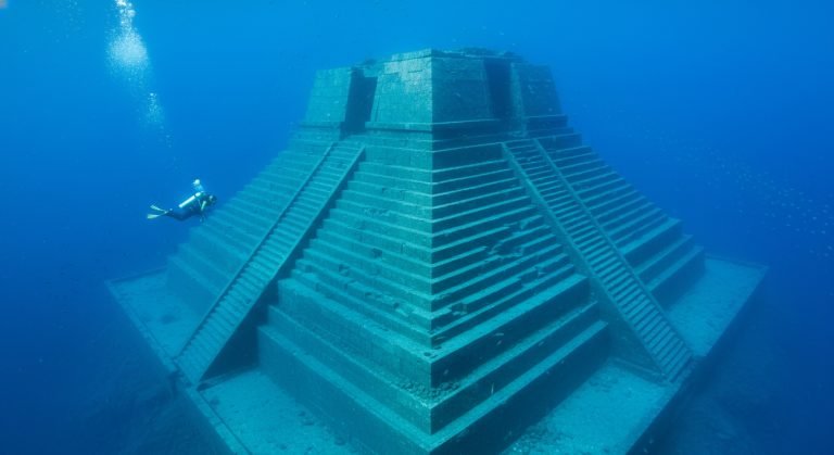 Vista submarina gran angular del Monumento de Yonaguni en Japón, mostrando sus inmensas terrazas de piedra y un buzo para escala.