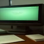Escritorio antiguo de madera con monitor clásico encendido, carpetas de archivo y una lupa bajo iluminación tenue de lámpara.